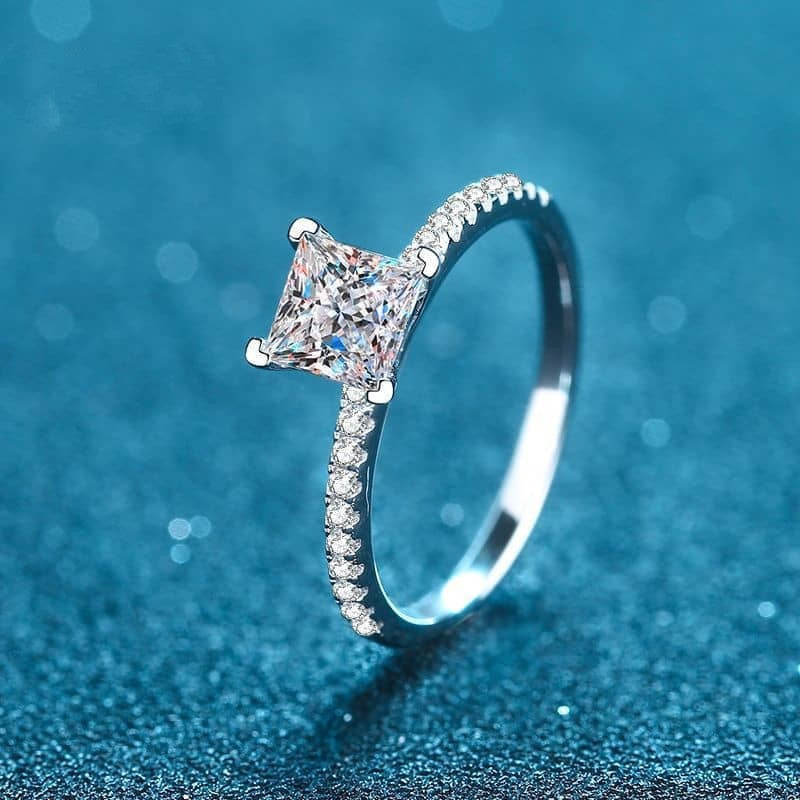 Princess cut moissanite Ring on pave band facing forward at an angle on blue background