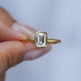 Hannah Emerald Cut Bezel Solitaire held between two fingers on a blurred background