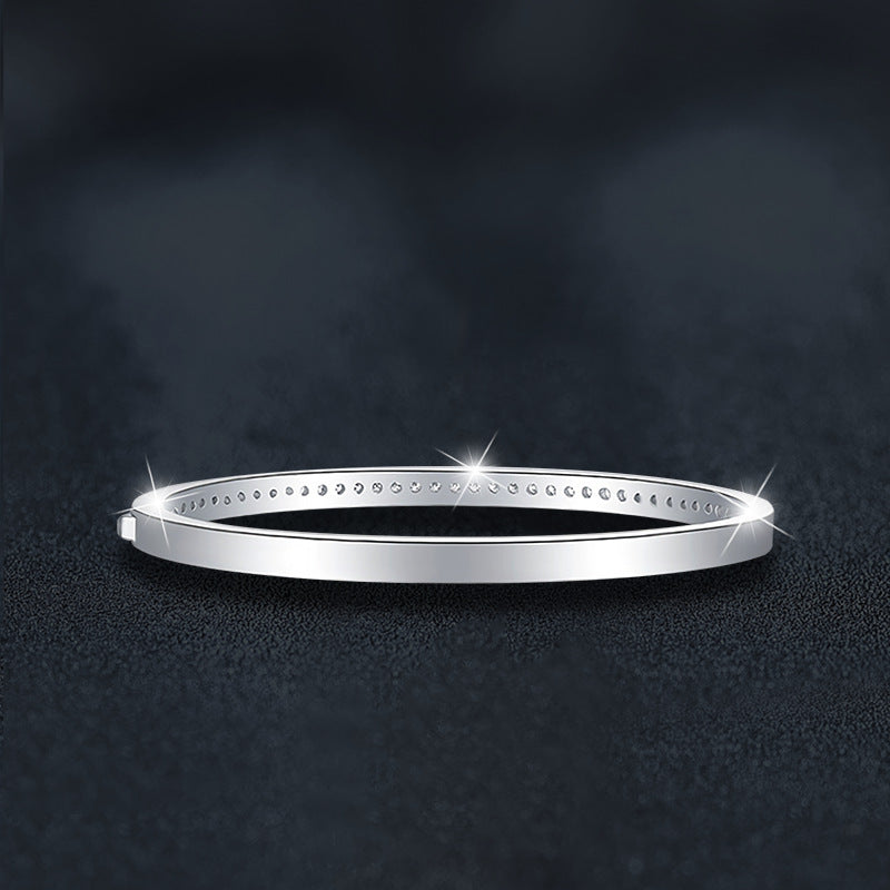 Silver bangle with small moissanite  stones showing the back of the brangle on a dark textured background