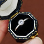 Diamond ring in a decorative black and gold box held by a hand. Prism and Pearl