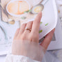 Hand wearing a gold ring with a blurred background of a magazine or book.