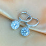 Silver hoop earrings with 1ct bezel set moissanites on a beige fabric background