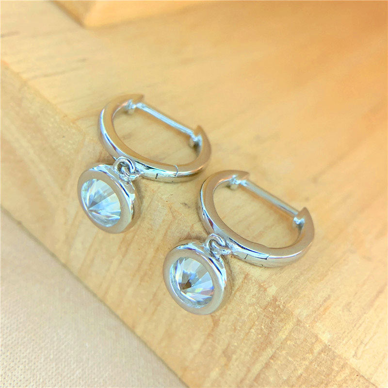Silver hoop earrings with 1ct bezel set moissanites dangling off a piece of wood